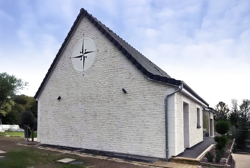 Bâtiment résidentiel moderne en brique blanche avec toit en tuiles noires, situé dans un environnement paysager avec arbres et végétation