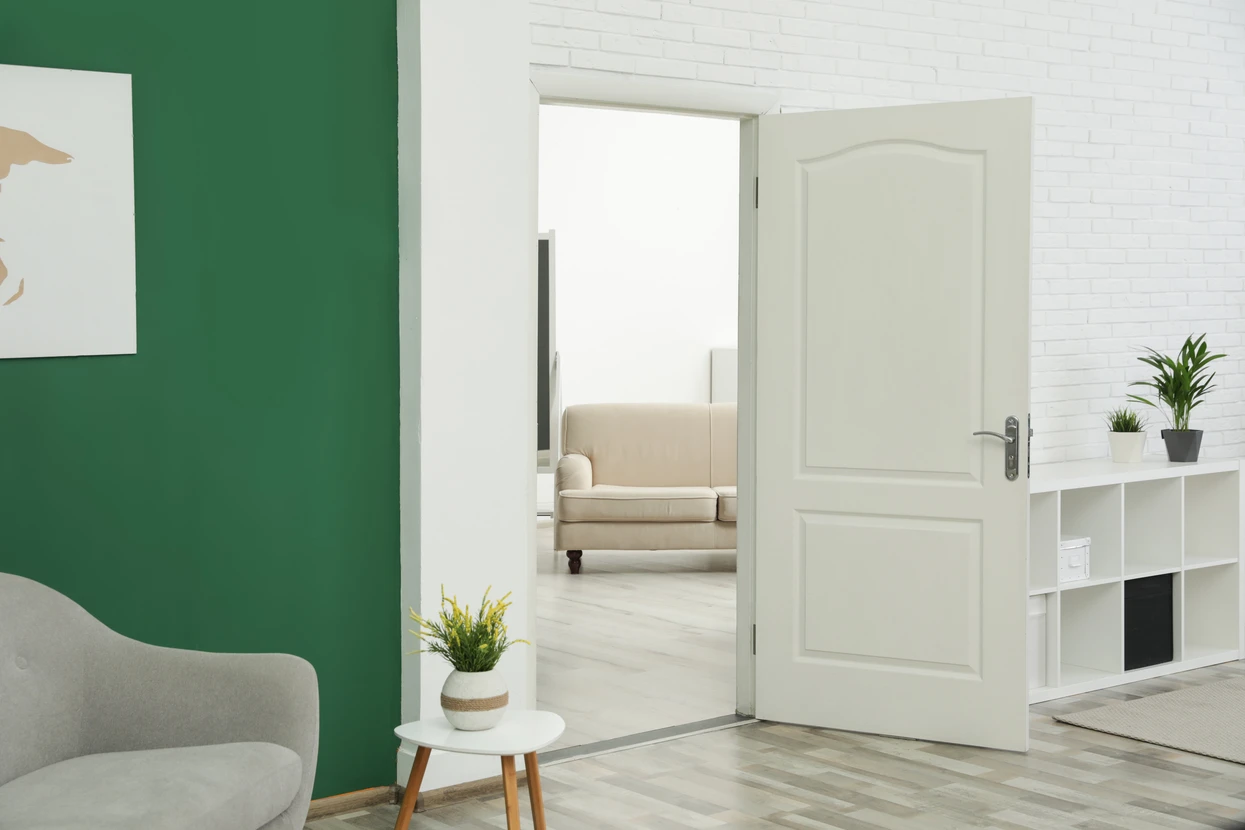 Intérieur résidentiel moderne avec mur d'accent vert émeraude, porte blanche ouverte révélant salon avec fauteuil beige