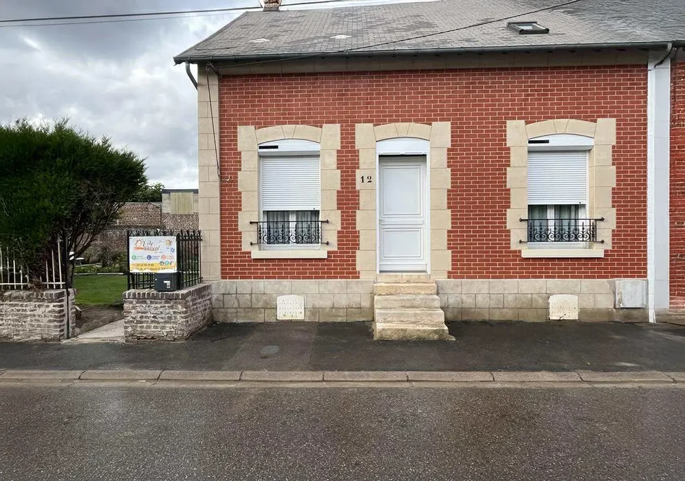 Façade de bâtiment moderne avec mur crépi beige, fenêtre circulaire ornementale à encadrement blanc en saillie, colonnes rectangulaires et porche couvert