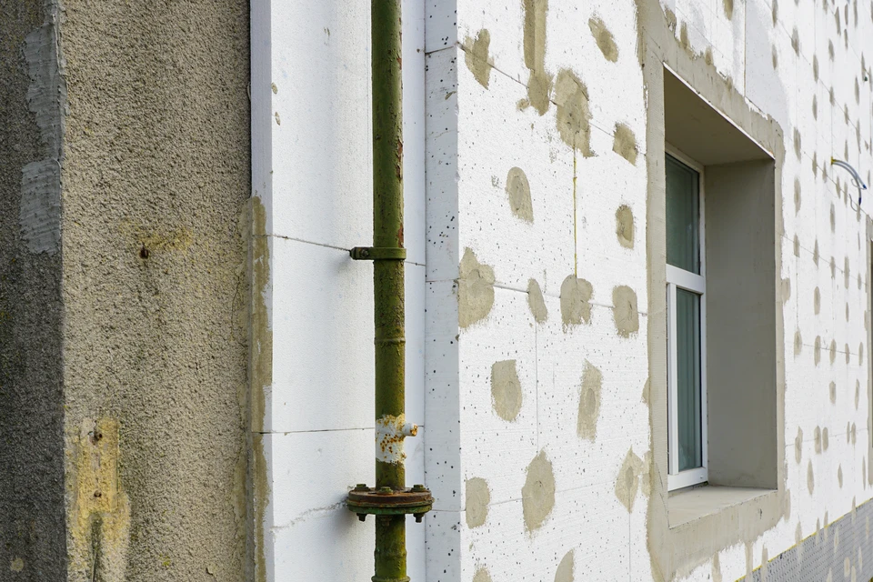 Deux ouvriers en vêtements haute visibilité installent des panneaux d'isolation thermique extérieure sur façade de maison individuelle
