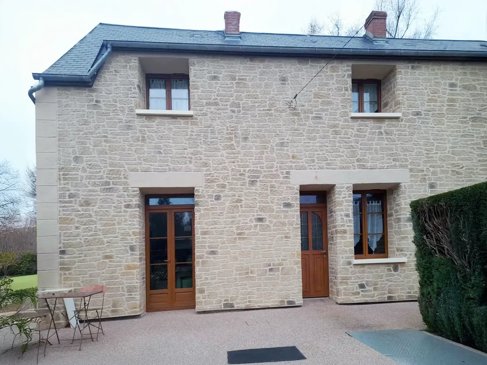 Maison moderne contemporaine à deux niveaux avec façade blanche et panneau vertical beige, située dans un environnement paysager verdoyant avec arbres matures et pelouse entretenue